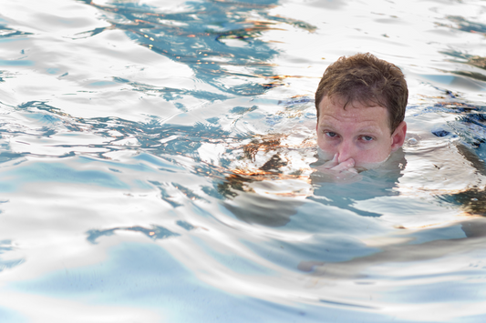 A man holding his nose as he swims.