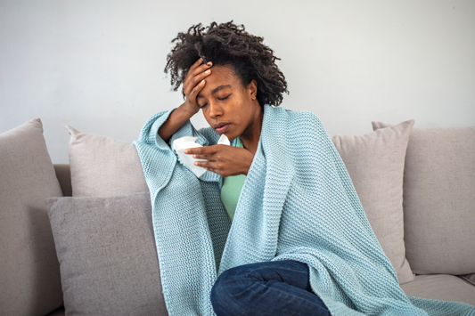 A woman with chest congestion blowing her nose on the couch.