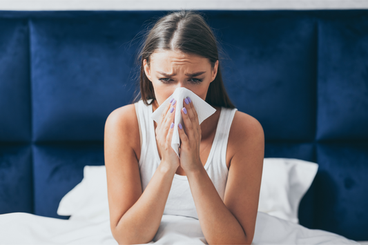 A young woman blowing her nose in bed after waking up with a stuffy nose.