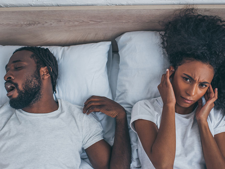Frustrated woman plugging ears against snoring husband in bed