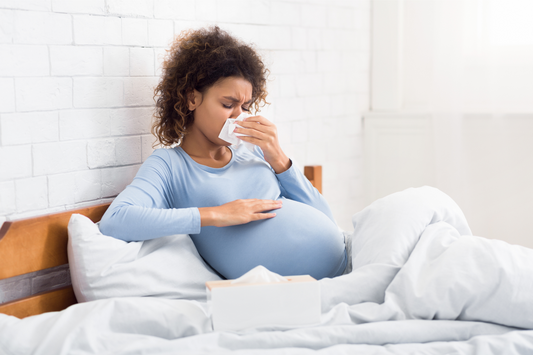 Pregnant woman with pregnancy rhinitis blowing her nose in bed.