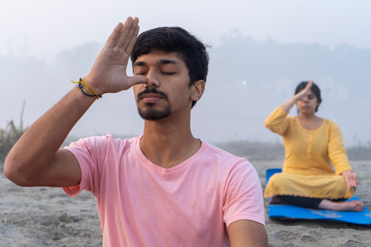 Two people practicing breathing exercises on the beach.