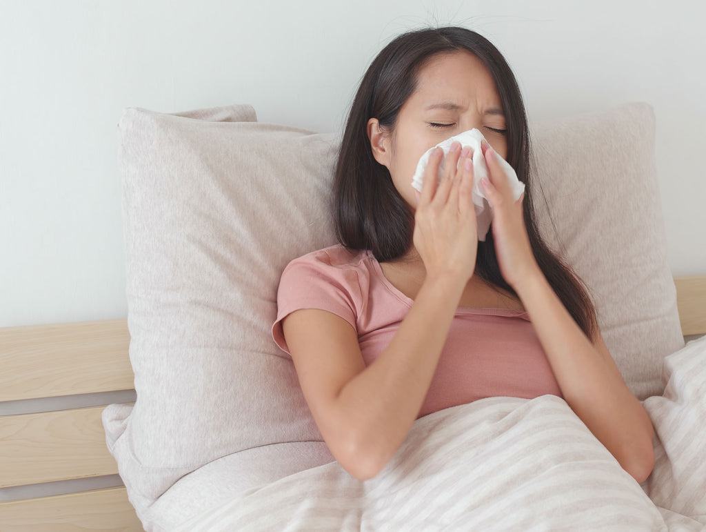 Woman with nighttime allergies blowing her nose in bed