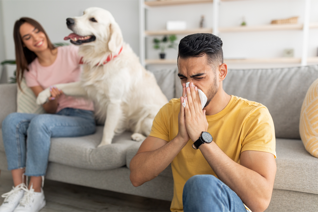 Young man with pet allergies blowing his nose next to a young woman and dog.