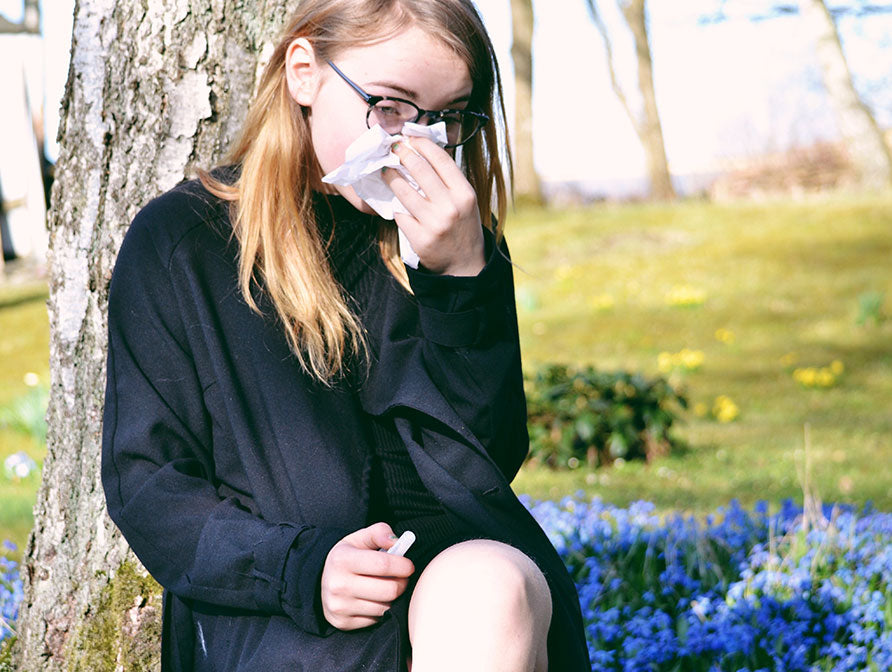 Young woman sitting against a tree blowing her nose