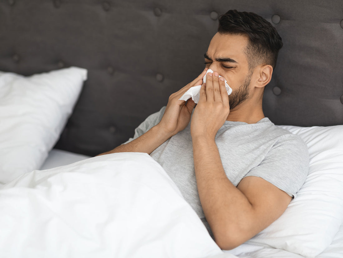 Man blowing nose into tissue while laying in bed